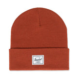 Rust-colored knit beanie with a folded cuff and a Herschel logo patch.