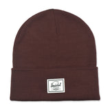 A brown knitted beanie hat with a folded cuff and a white label featuring the brand name "Herschel."
