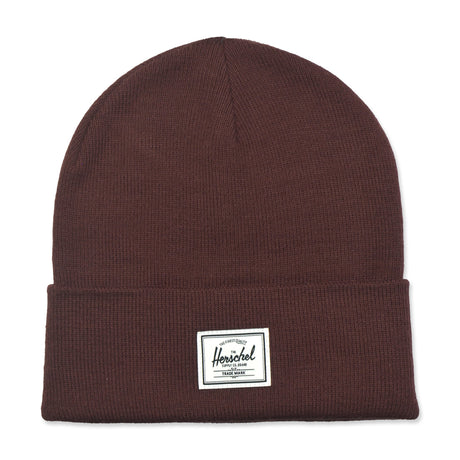 A brown knitted beanie hat with a folded cuff and a white label featuring the brand name "Herschel."