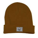 A mustard-colored beanie hat with a folded cuff and a white Herschel brand label.