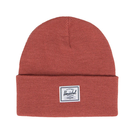 A rust-colored knit beanie with a folded cuff and a small rectangular tag that says "Herschel" on it.
