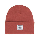 A rust-colored knit beanie with a folded cuff and a small rectangular tag that says "Herschel" on it.