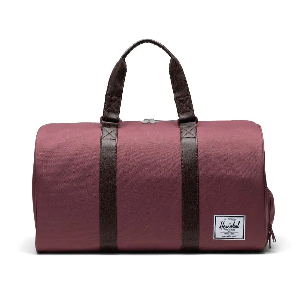A maroon duffel bag with dark brown straps and a side zipper, featuring a white Herschel label.