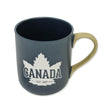 A navy blue ceramic mug with a beige handle, featuring a white maple leaf and the word "CANADA" along with "EST 1867" printed on the front.