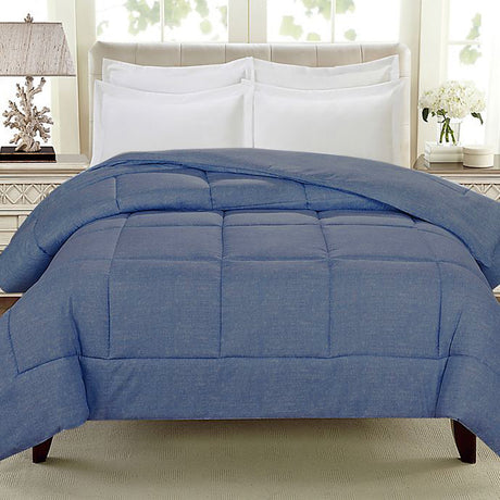 A neatly made bed with a blue quilt and white pillows against a light-colored headboard, with a bedside lamp and decorative elements in the background.