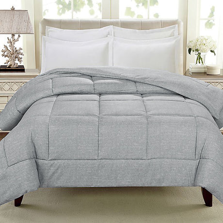 Gray comforter draped over a bed with white pillows and a bedside lamp, in a well-lit room with large windows.