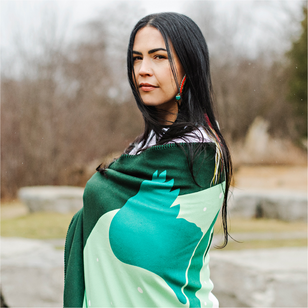 Indigenous student wrapped in teal blanket from the Indigenous Collection standing outside